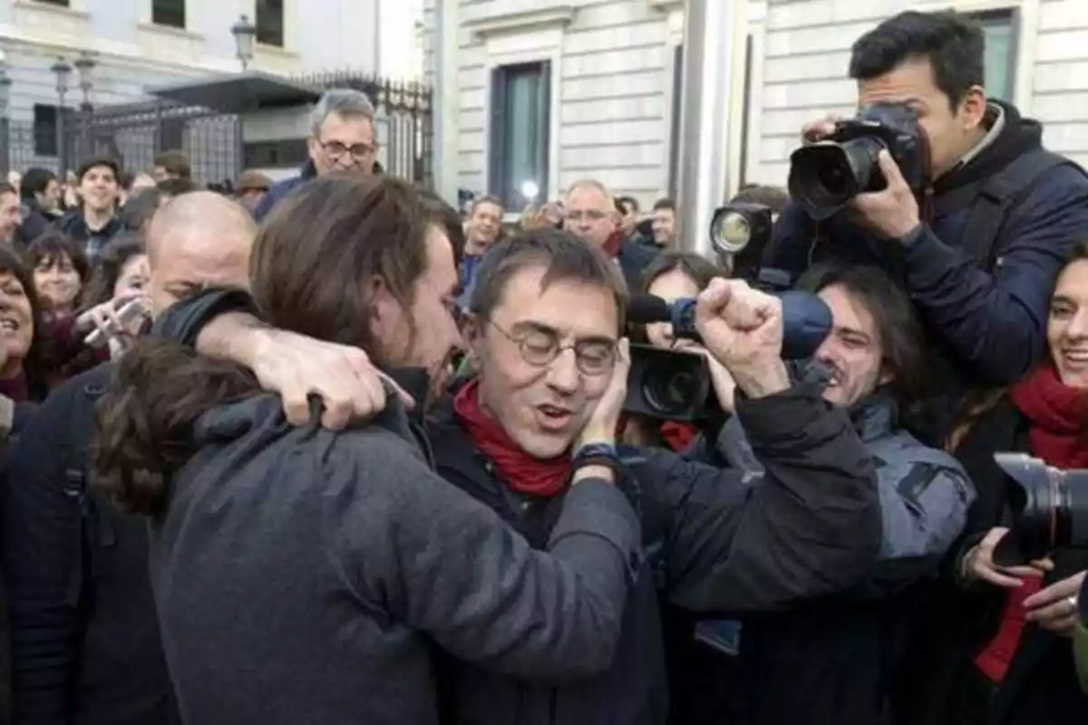 Un grupo de personas se abraza y celebra mientras son fotografiados y filmados por varios reporteros en una calle concurrida.