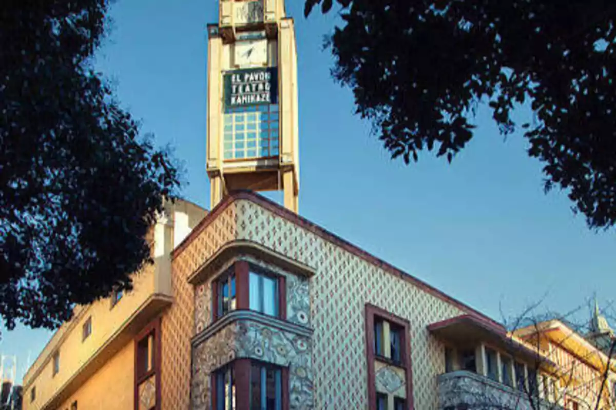 Edificio de estilo arquitectónico clásico con una torre de reloj en la parte superior, rodeado de árboles y con un cielo despejado.