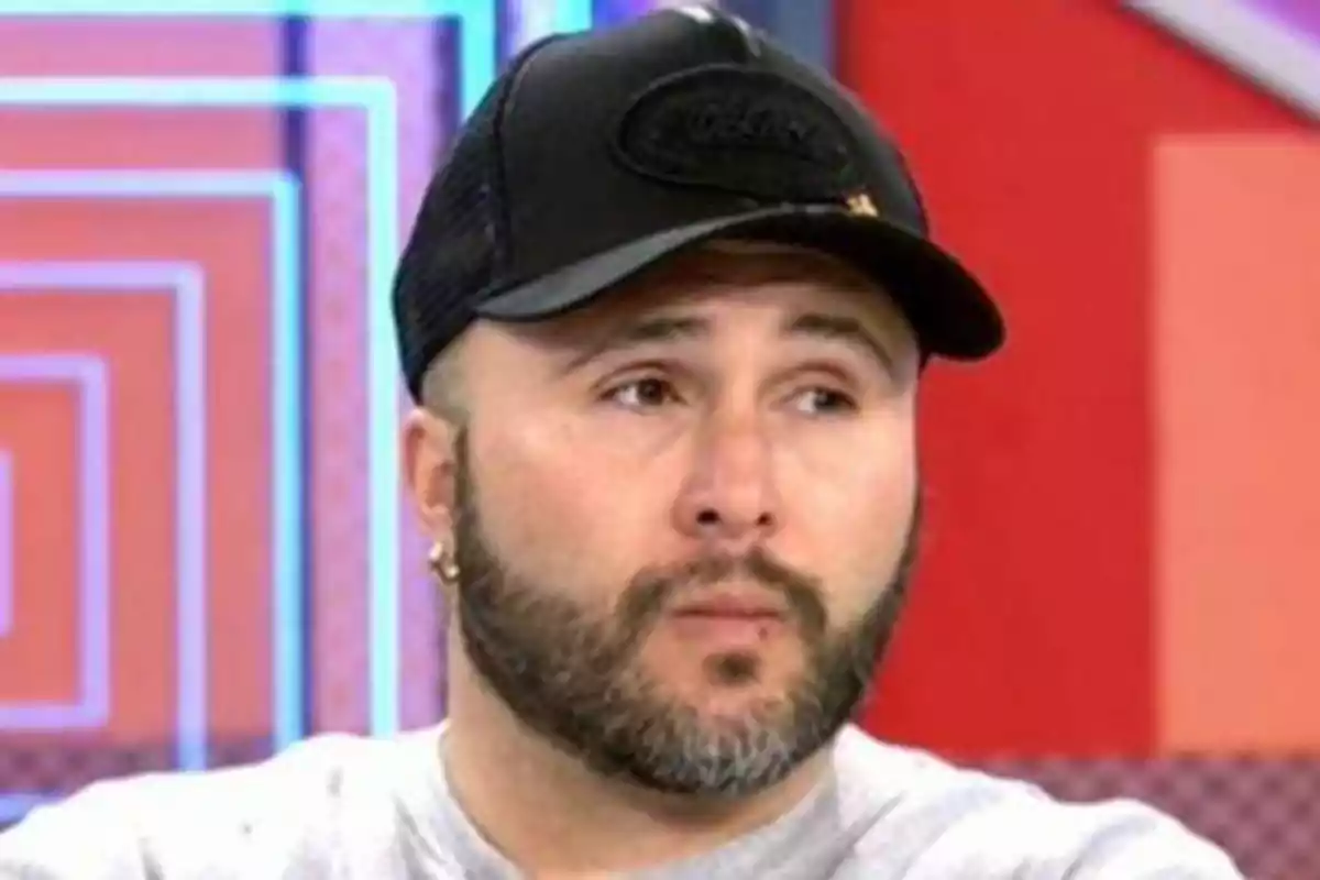 Hombre con barba y gorra negra en un entorno colorido.