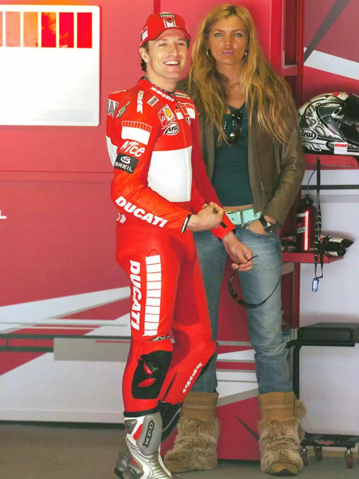 Un piloto de motociclismo con traje rojo de Ducati sonríe junto a una mujer rubia en un garaje.