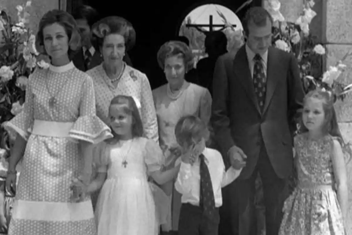 Una familia posando para una foto en blanco y negro, con adultos y niños vestidos de manera formal, de pie frente a una iglesia decorada con flores.
