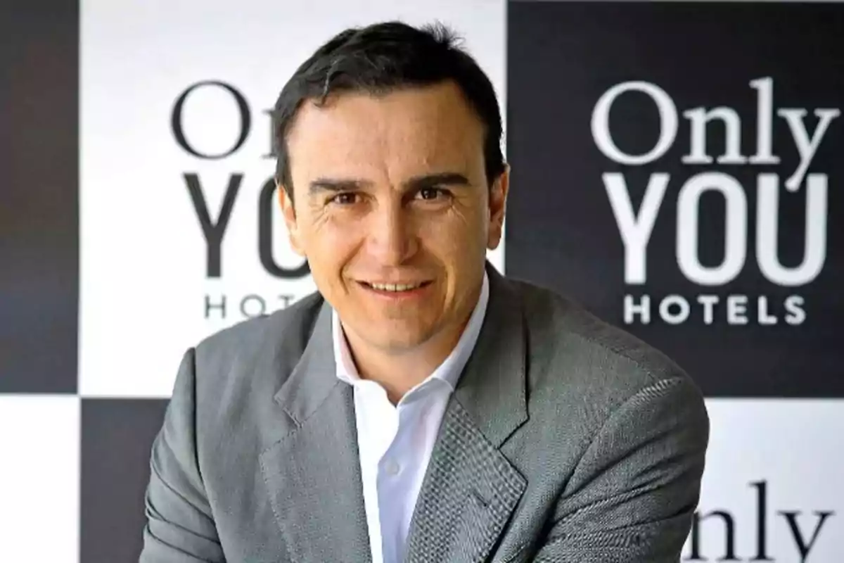 Hombre con traje gris sonriendo frente a un fondo con el logo de Only YOU Hotels.