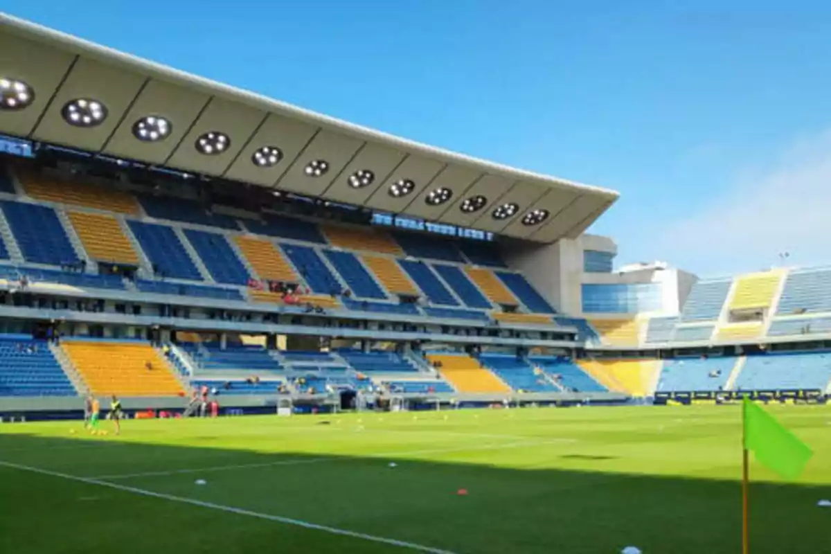 Estadio de fútbol vacío con gradas azules y amarillas y una bandera de esquina verde