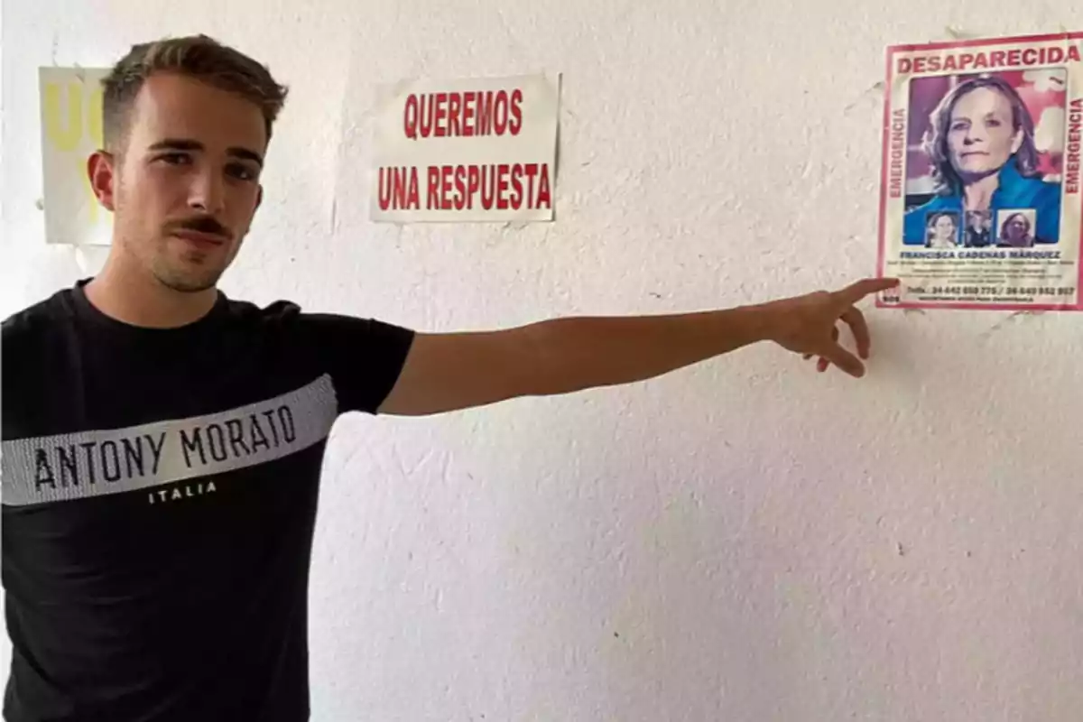 Un hombre señala un cartel de persona desaparecida en una pared blanca donde también hay un letrero que dice Un hombre señala un cartel de persona desaparecida en una pared blanca donde también hay un letrero que dice