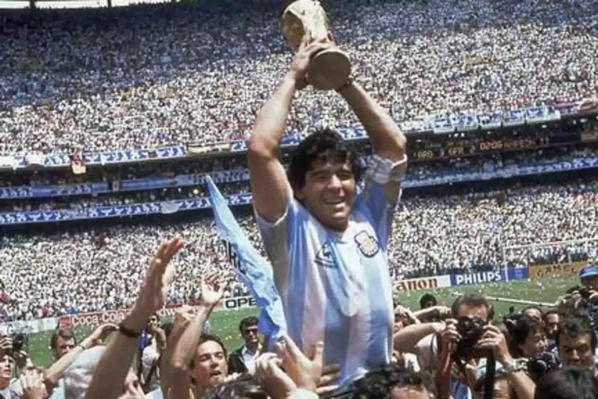 Un jugador de fútbol argentino levanta un trofeo mientras es celebrado por una multitud en un estadio lleno.