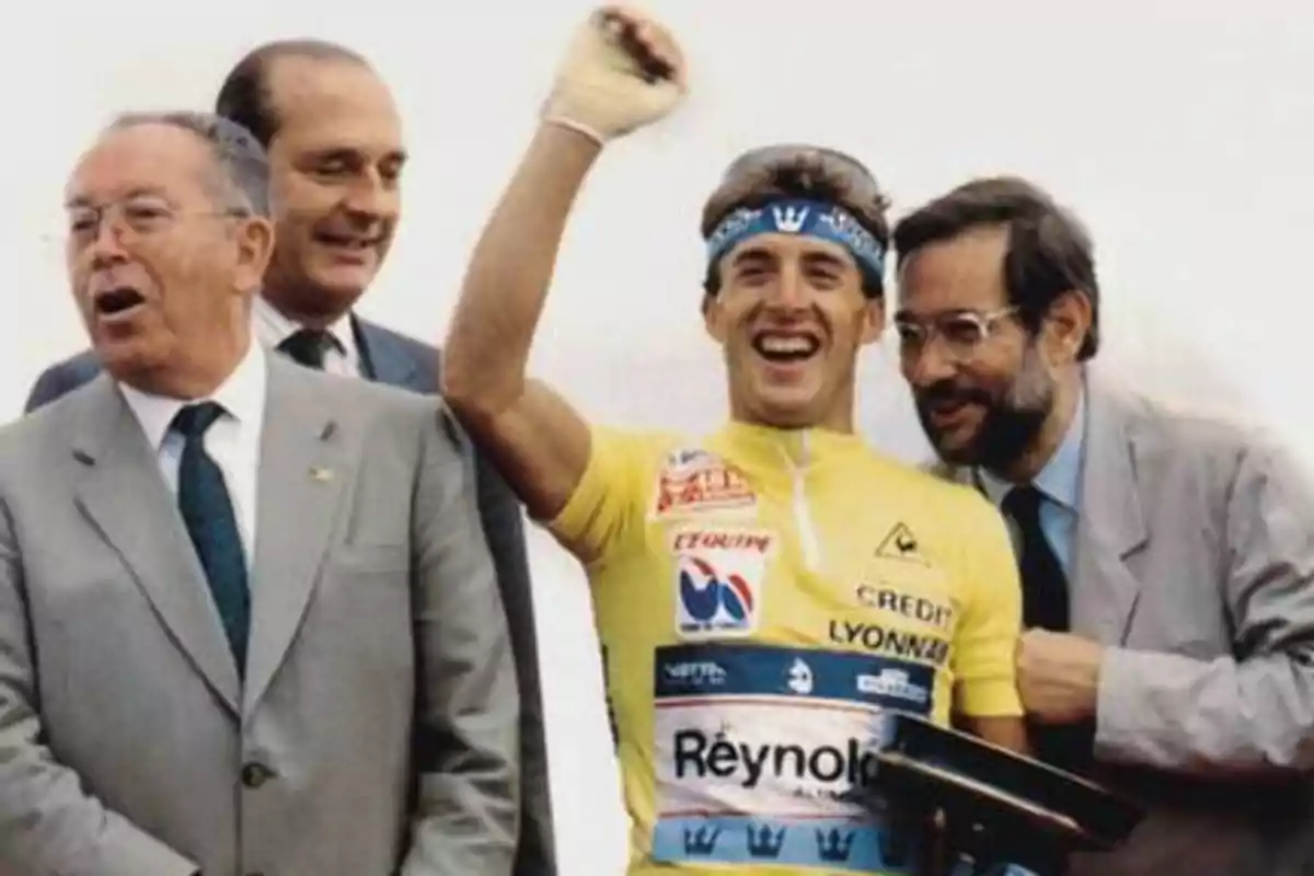 Un ciclista celebrando con tres hombres de traje a su alrededor.