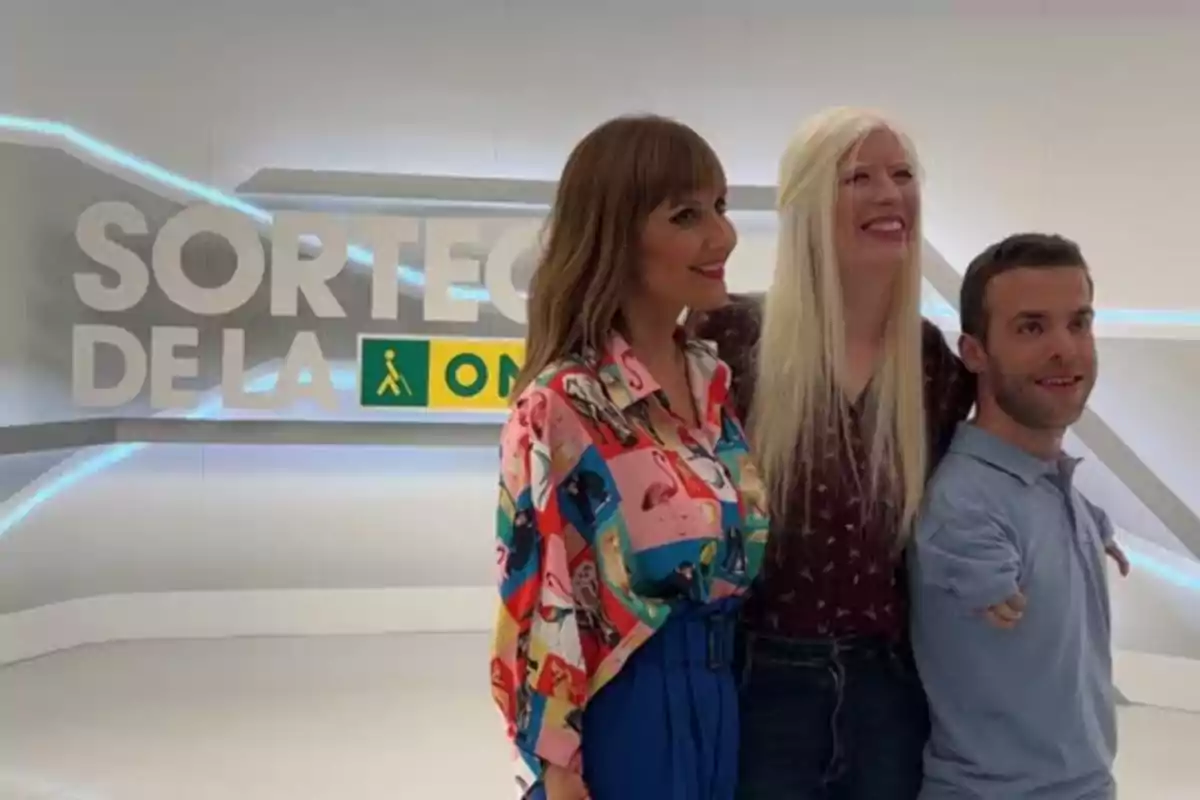 Tres personas posan juntas frente a un cartel que dice 