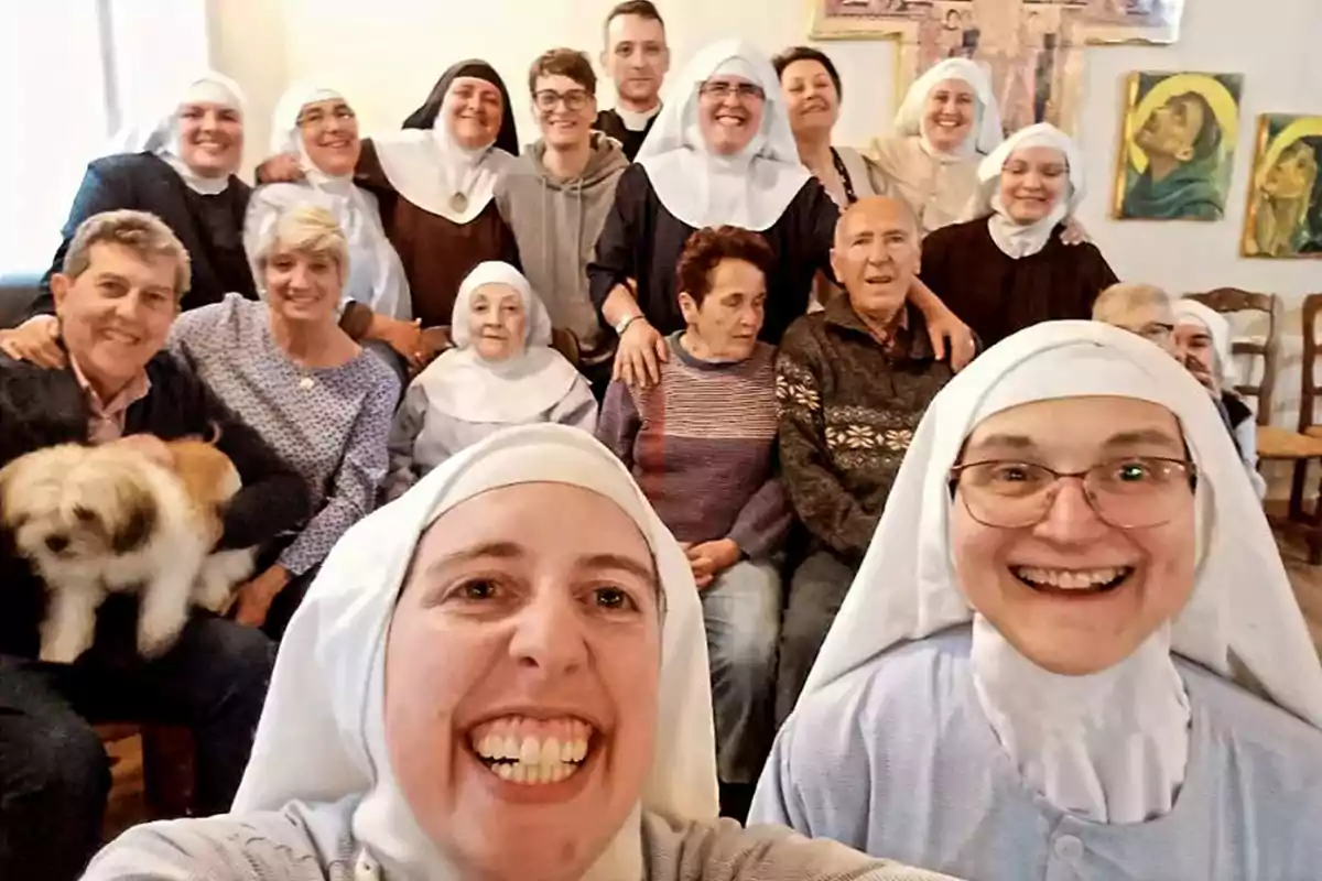 Un grupo de personas, incluyendo monjas y laicos, posando para una foto grupal en un ambiente interior, con algunas de ellas sonriendo y un perro pequeño en el regazo de una persona.