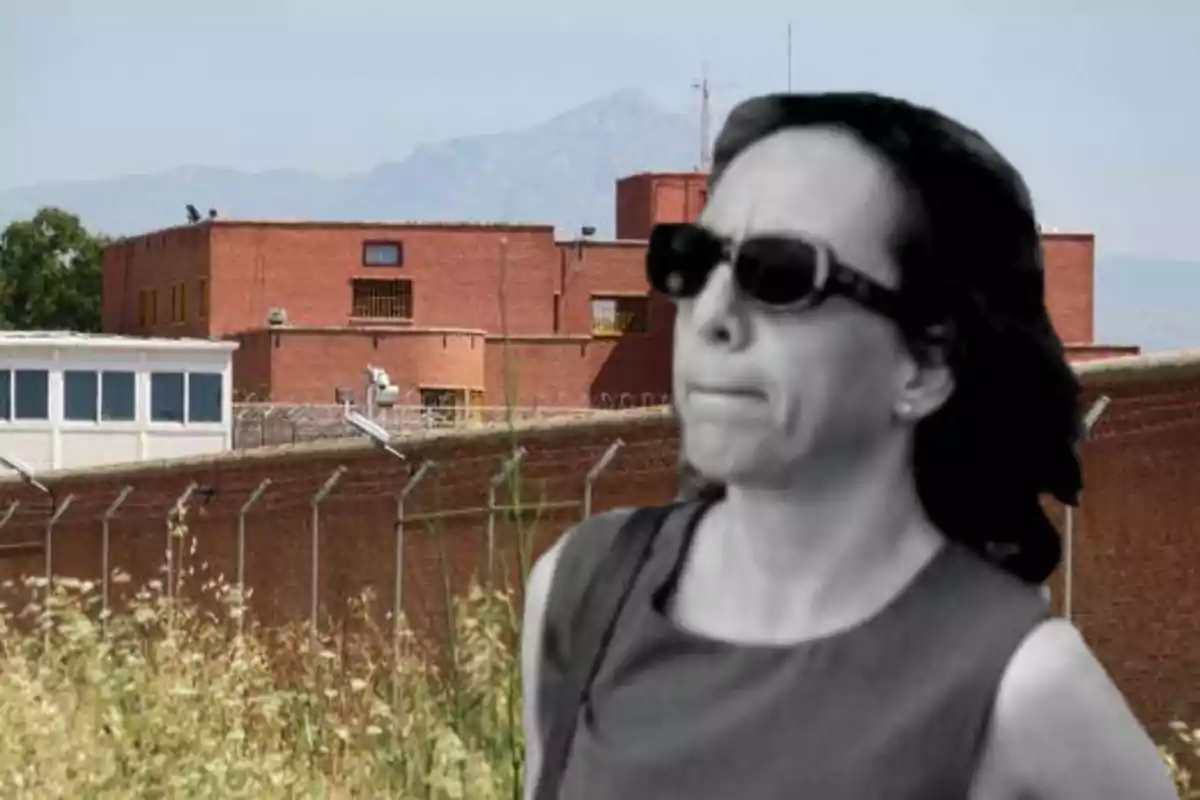 Una mujer con gafas de sol frente a un edificio de ladrillo con una cerca de alambre de púas.