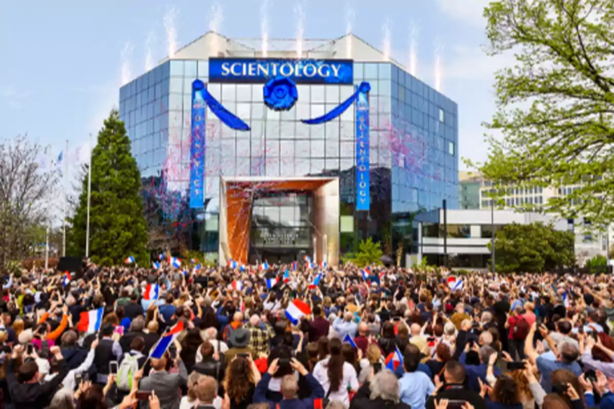 Una multitud se reúne frente a un edificio de Scientology decorado con cintas y fuegos artificiales.