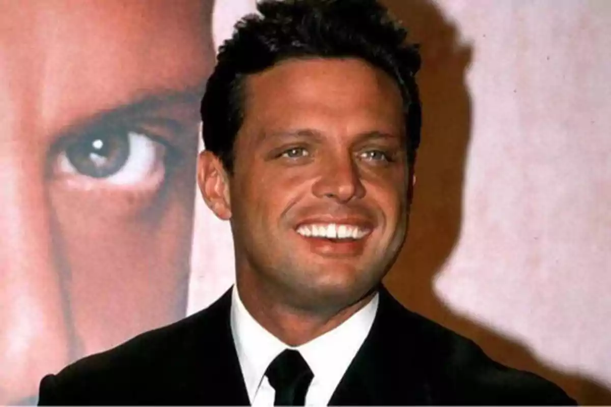 Hombre sonriendo con traje y corbata frente a un fondo con una imagen de un ojo.