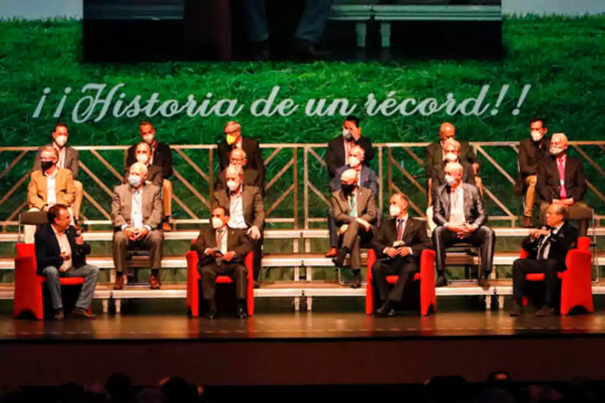 Un grupo de personas sentadas en un escenario con un fondo verde y un letrero que dice "¡Historia de un récord!".