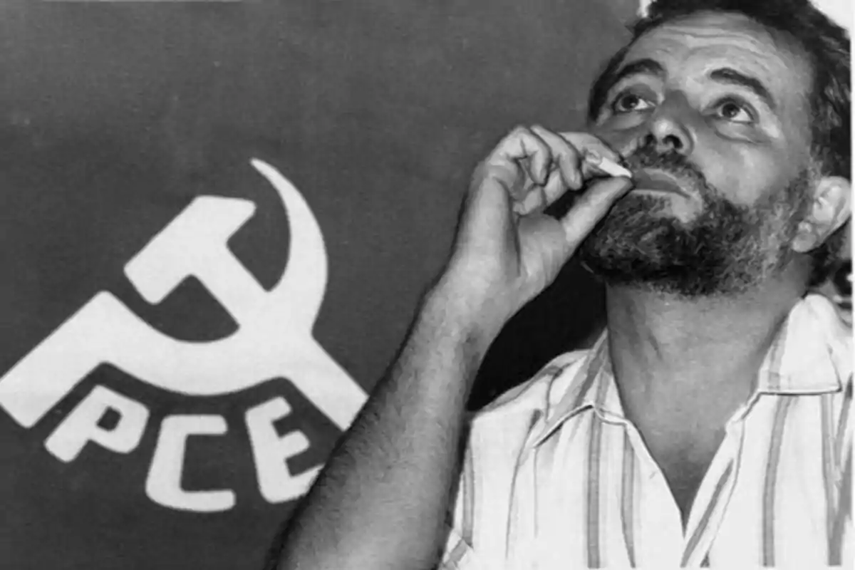 Un hombre con barba y camisa de rayas sostiene un cigarrillo cerca de su boca, con un fondo que muestra el logotipo del Partido Comunista de España (PCE).