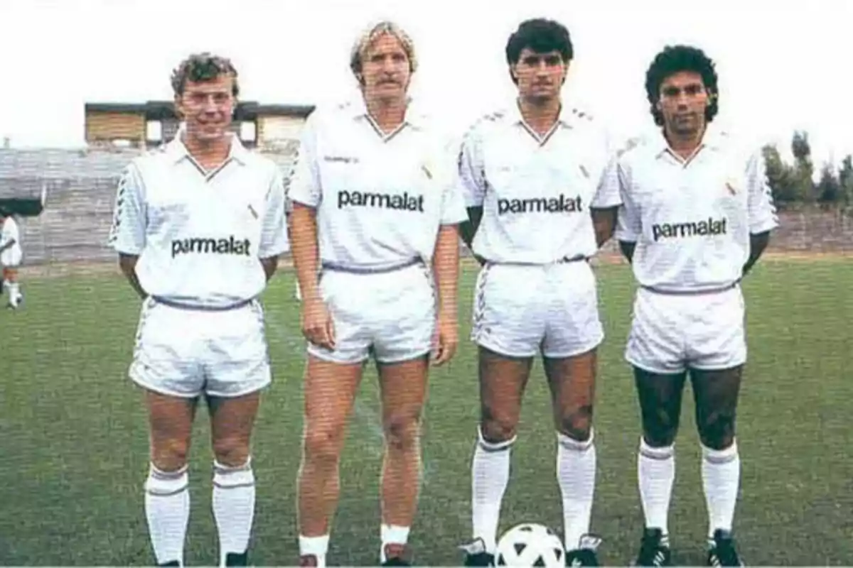 Cuatro jugadores de fútbol con uniforme blanco de Parmalat posando en un campo de fútbol.