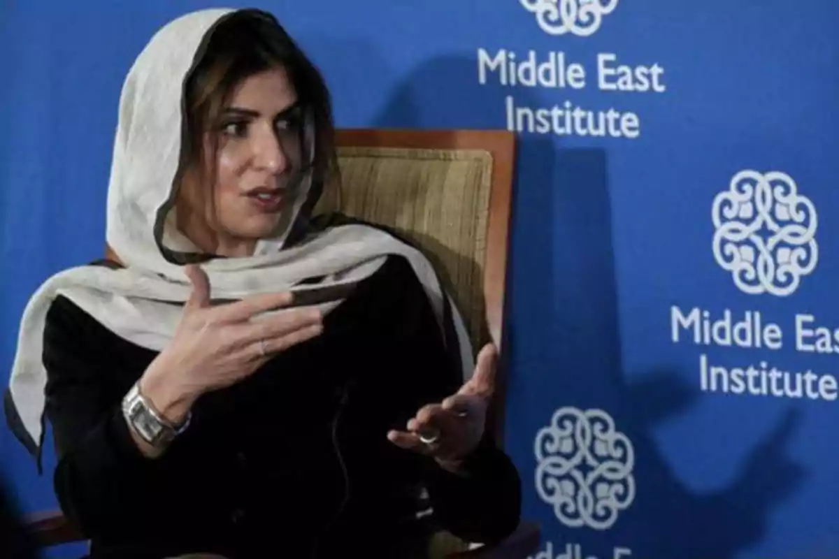 Una mujer con un pañuelo en la cabeza está hablando y gesticulando con las manos, sentada frente a un fondo azul con el logotipo y el nombre del Middle East Institute.