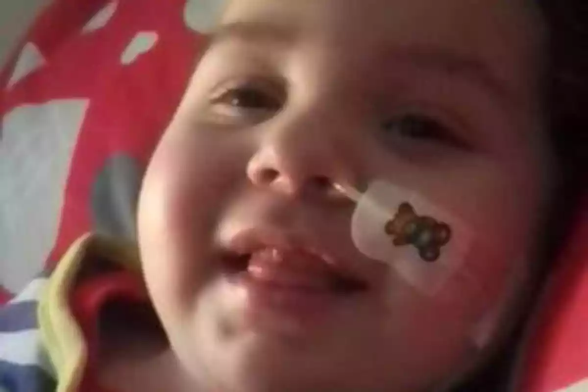 Un niño sonriente con una sonda nasogástrica y una tirita con un dibujo de osito en la mejilla.