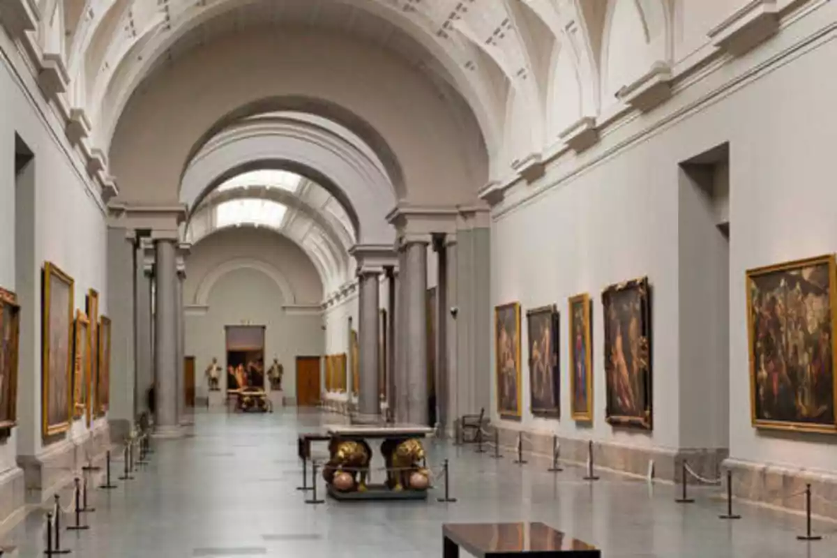 Un pasillo de un museo con techos altos y arcos, decorado con columnas y cuadros en las paredes.