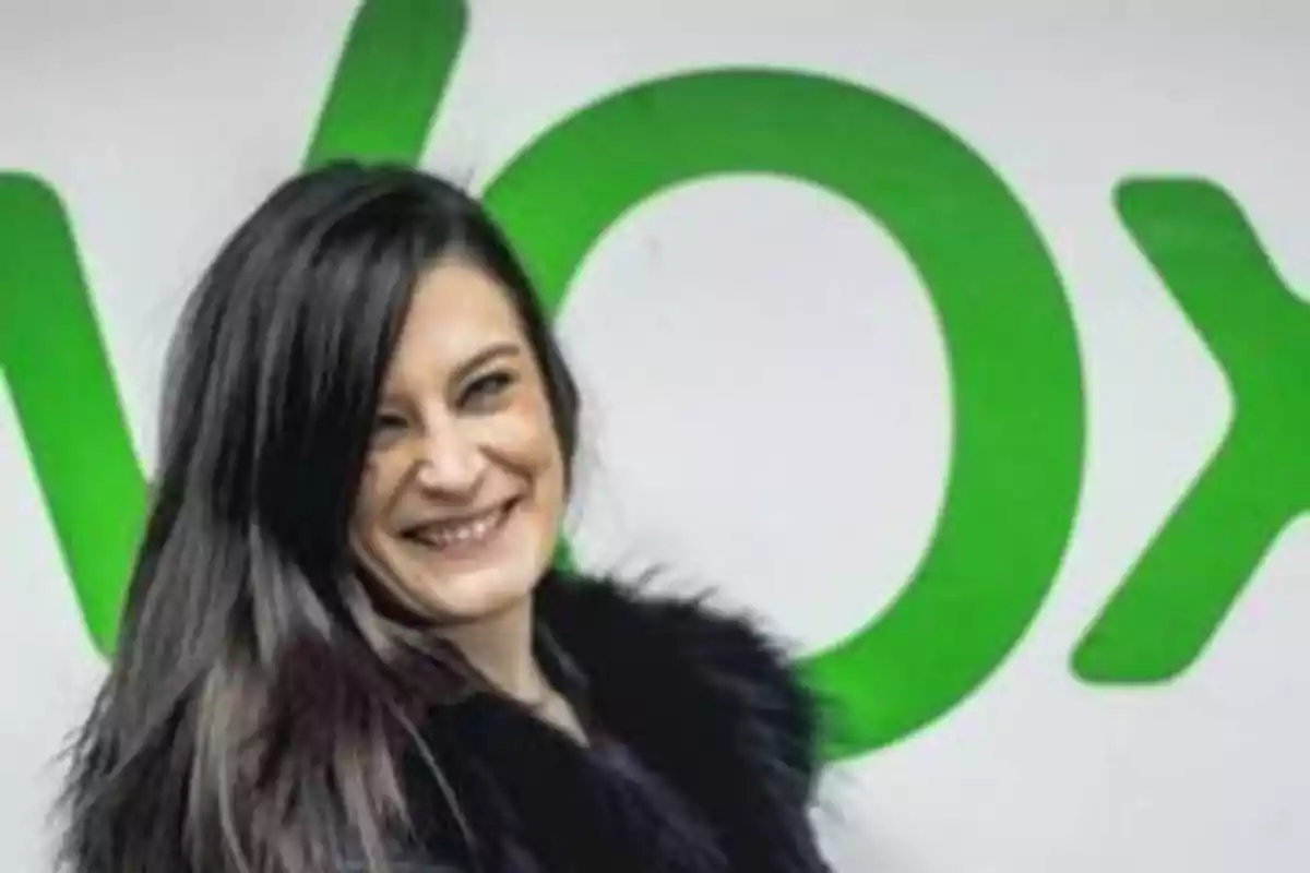 Mujer sonriendo frente a un cartel con letras verdes.