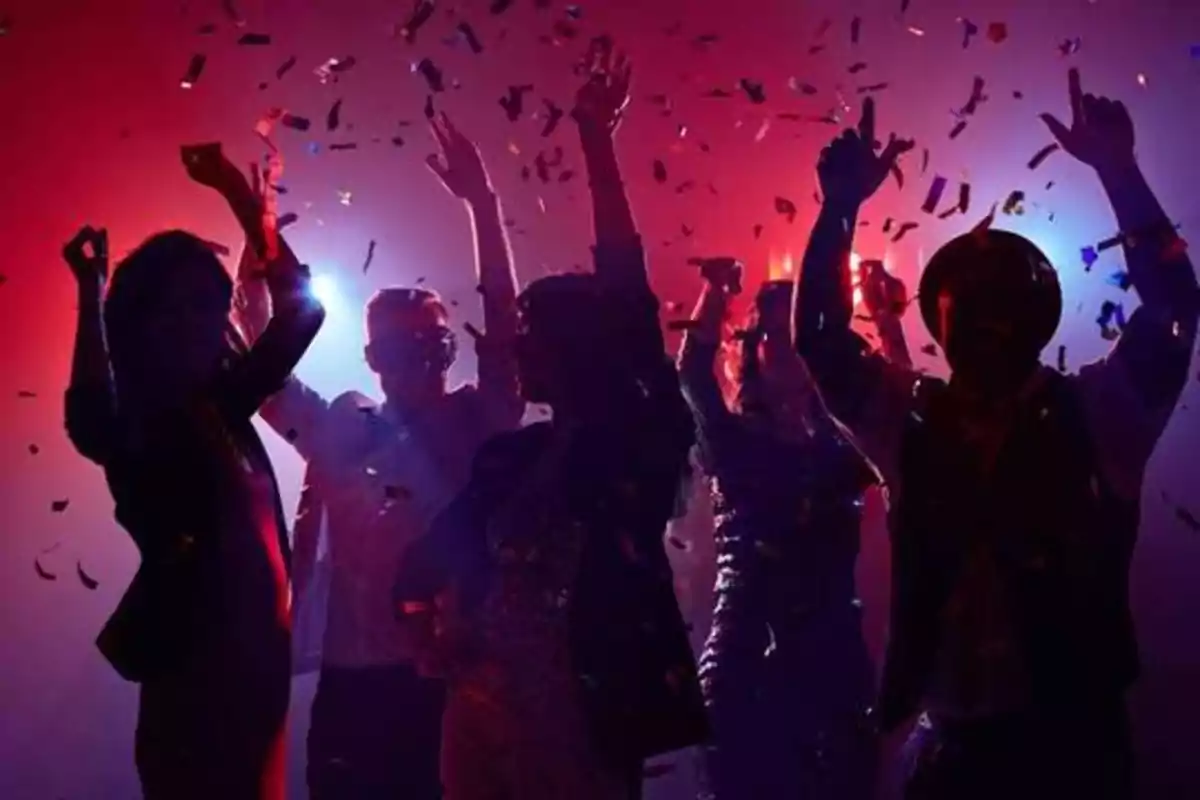 Personas bailando y celebrando en una fiesta con confeti y luces de colores.