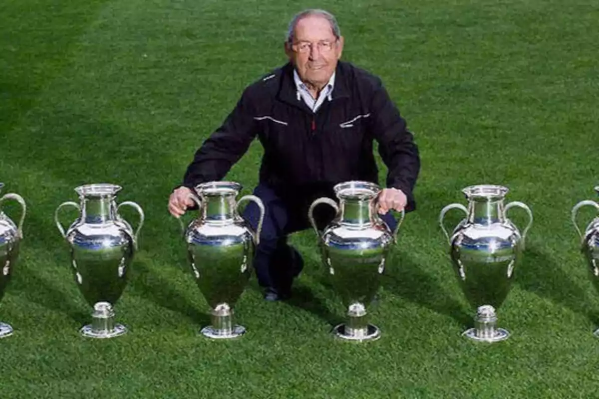 Un hombre mayor posando en un campo de césped con cinco trofeos idénticos.