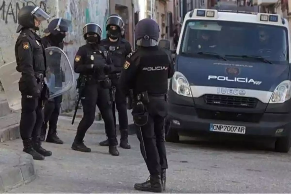 Un grupo de policías con equipo antidisturbios se encuentra en una calle junto a una furgoneta policial.