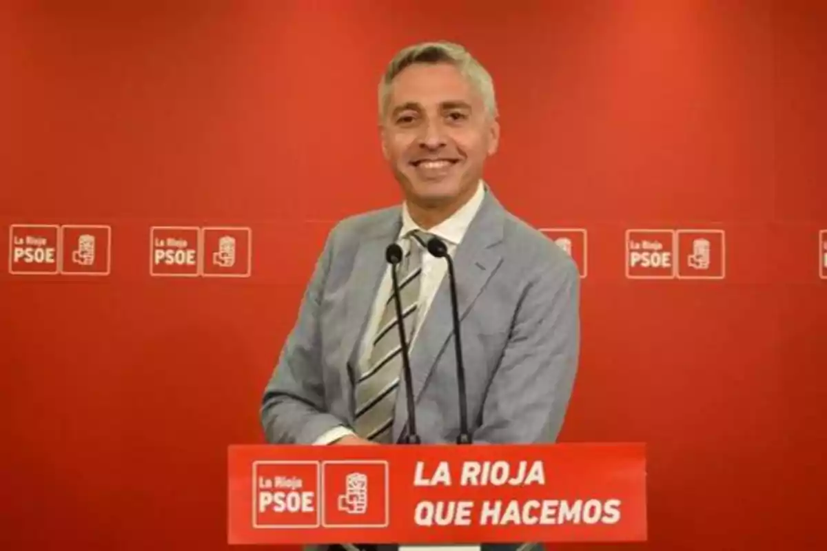 Hombre de pie detrás de un podio rojo con el logotipo del PSOE de La Rioja y el texto "LA RIOJA QUE HACEMOS"