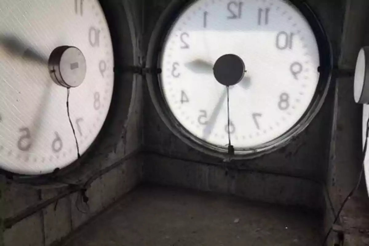 Vista interior de una torre de reloj con dos grandes esferas de reloj iluminadas desde atrás mostrando números y agujas.