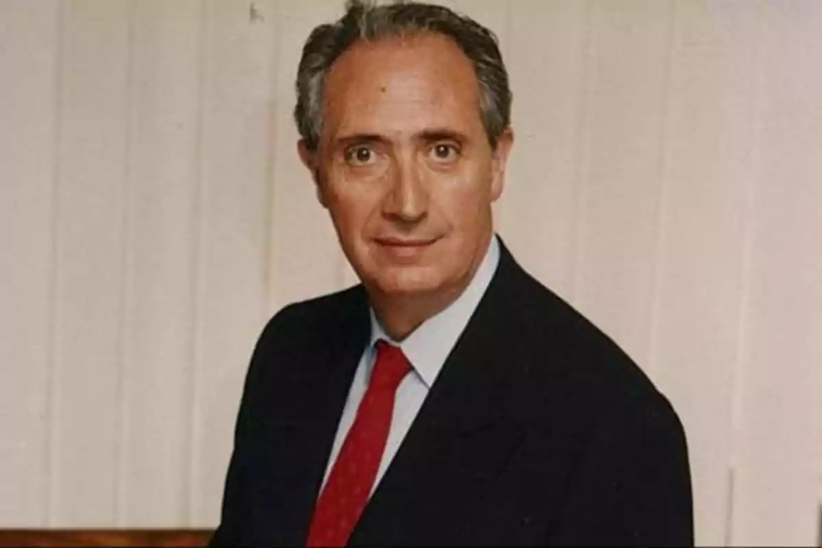 Hombre de cabello canoso con traje oscuro y corbata roja posando frente a un fondo claro.