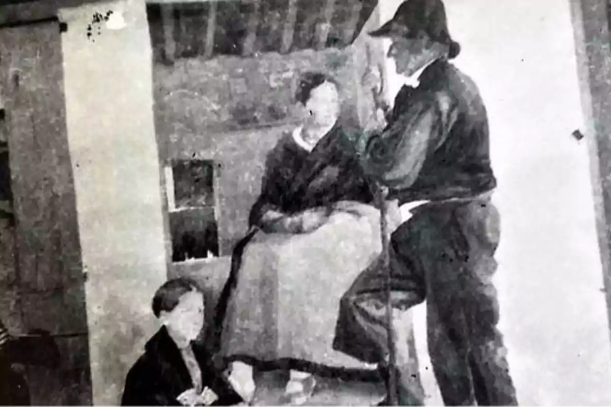 Una pintura en blanco y negro muestra a tres personas en una escena interior, con una mujer sentada en el centro, un hombre de pie a la derecha y un niño a la izquierda.