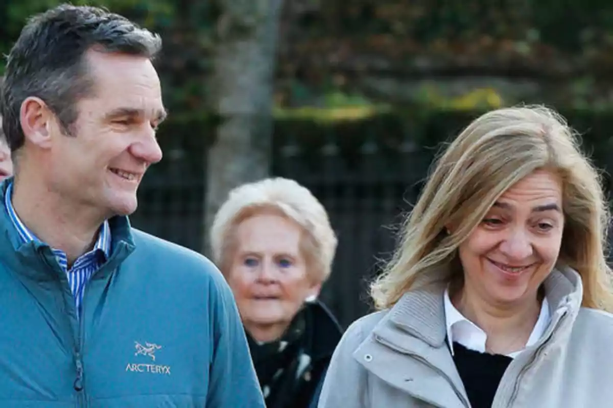 Dos personas sonrientes caminando al aire libre con una persona mayor en el fondo.