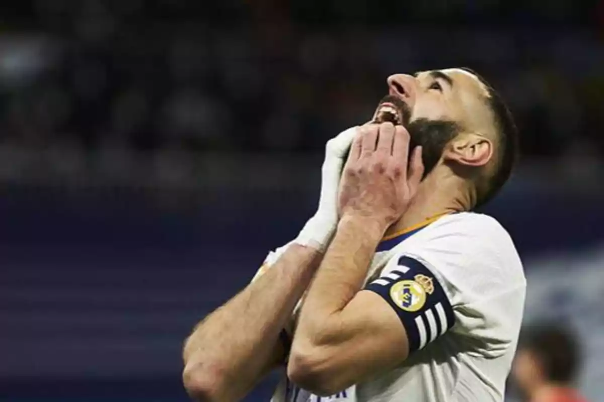 Jugador de fútbol con uniforme blanco y brazalete de capitán, con expresión de frustración y manos en la cara.