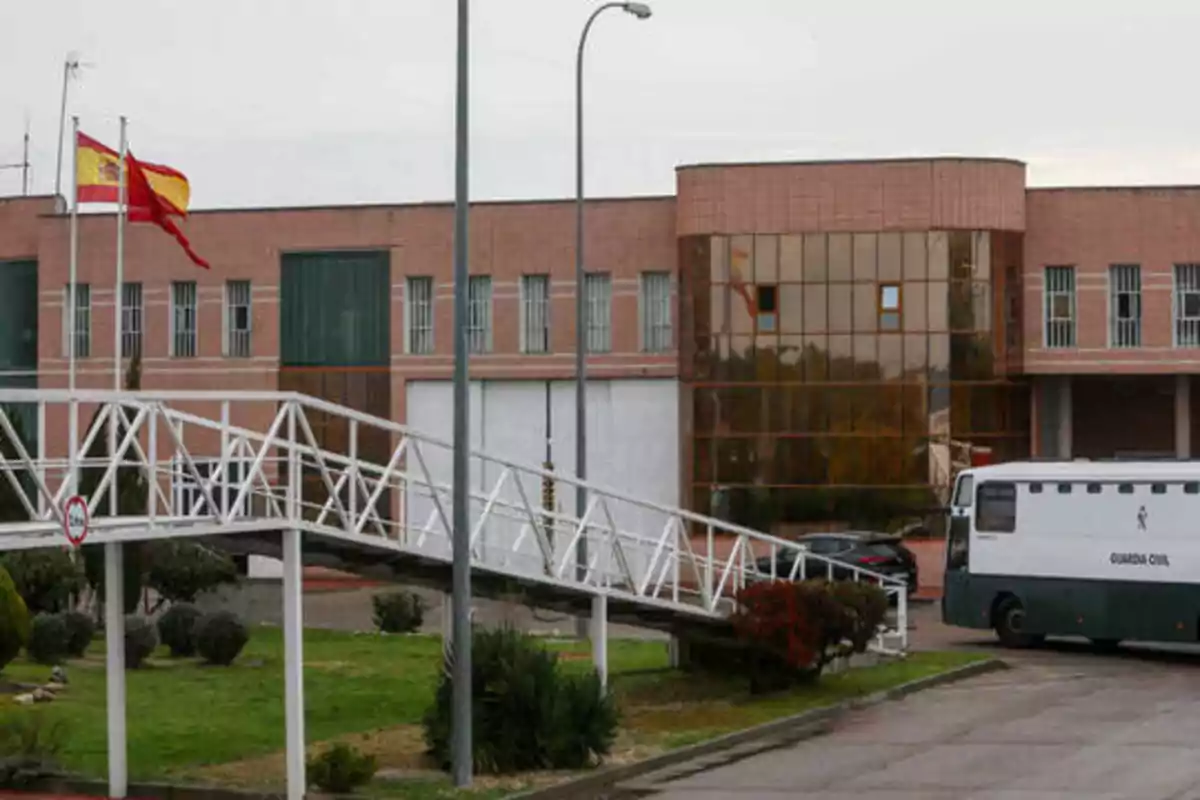 Edificio de ladrillo con ventanas y una estructura de vidrio, con una rampa blanca en primer plano y un autobús de la Guardia Civil estacionado.