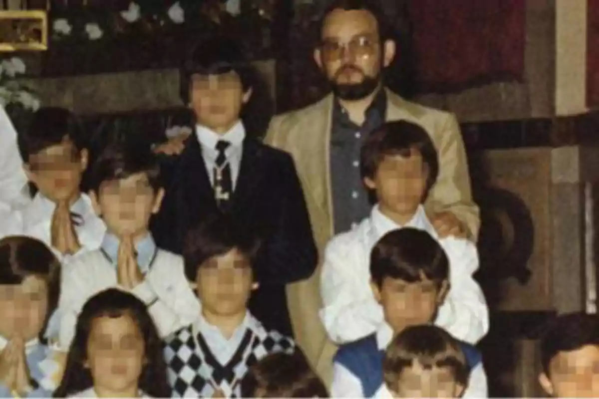 Un grupo de niños con los rostros pixelados posando junto a un hombre adulto con barba y gafas en un entorno interior.