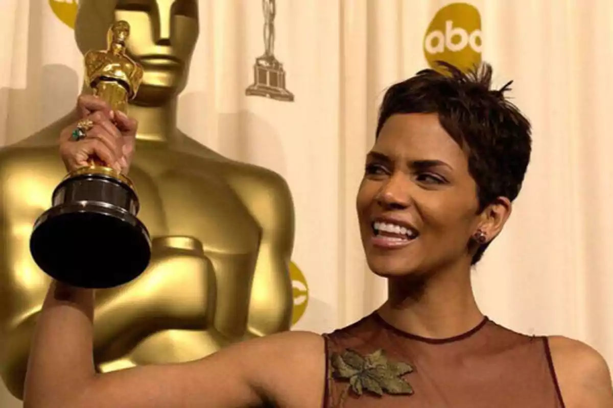 Una persona sosteniendo un premio Oscar con una gran estatua dorada de fondo.