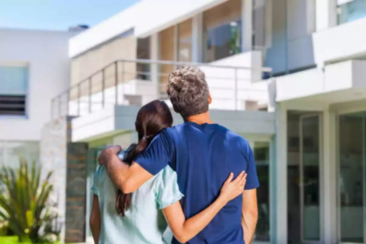 Una pareja abrazada de espaldas mirando una casa moderna.