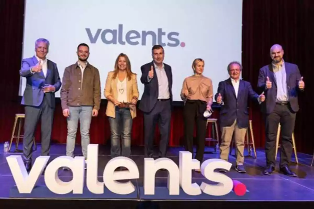 Un grupo de personas posando en un escenario con el logo de "valents" al fondo y en letras grandes frente a ellos.