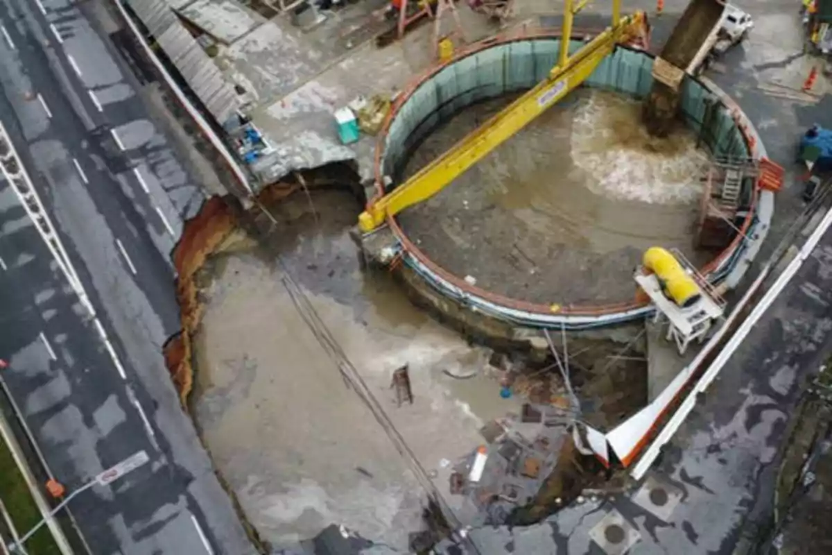 Una vista aérea de un gran socavón en una calle, con maquinaria de construcción y equipos trabajando en el área afectada.