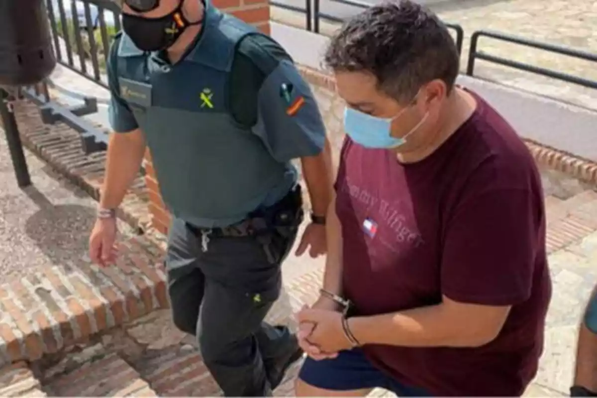 Un agente de la Guardia Civil escolta a un hombre esposado que lleva una camiseta roja y una mascarilla.