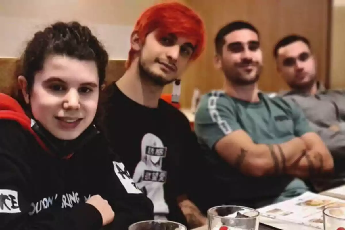 Un grupo de cuatro personas sentadas en una mesa, con bebidas y menús frente a ellos, posando para la cámara en un ambiente informal.