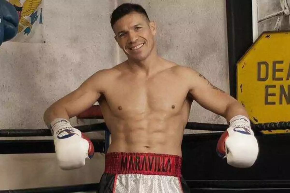 Boxeador sonriente con guantes y pantalones cortos de boxeo en un gimnasio.