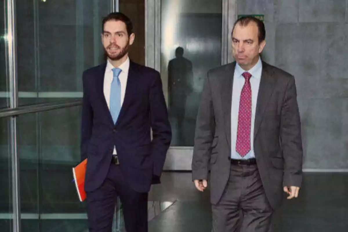 Dos hombres con trajes formales caminando por un pasillo.