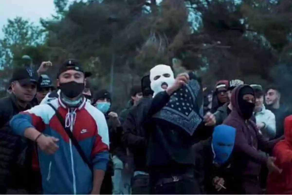 Un grupo de personas con máscaras y ropa casual se encuentra reunido al aire libre, algunas de ellas levantando pañuelos y otras con capuchas y gorras.