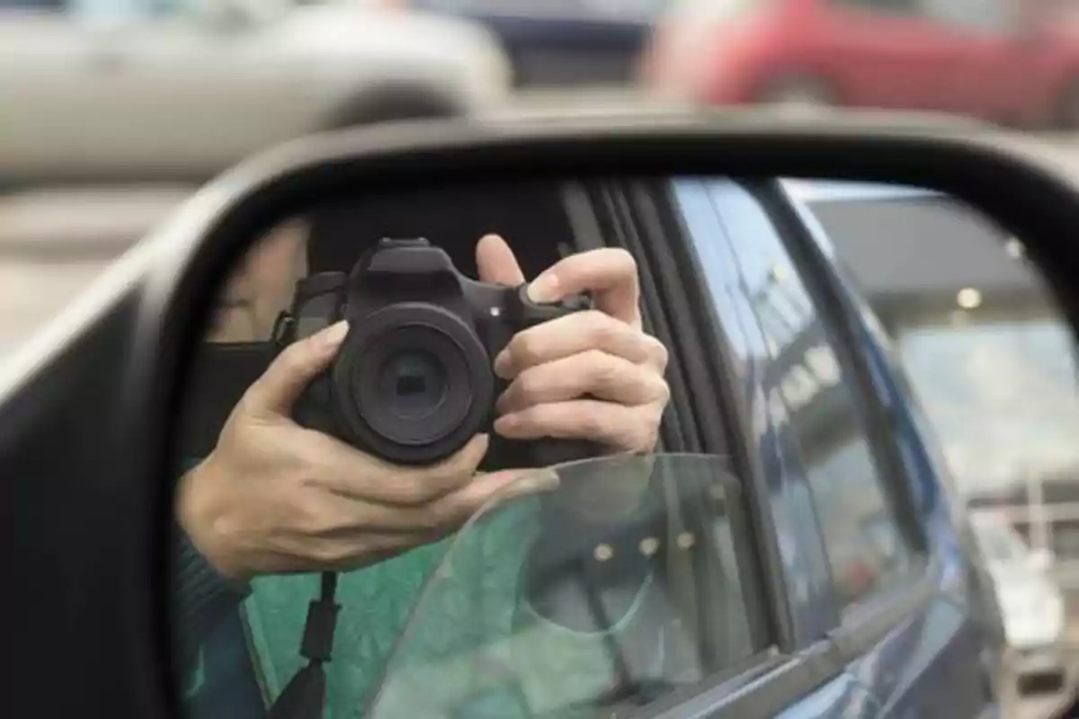 Reflejo de una persona tomando una foto con una cámara en el espejo lateral de un automóvil.