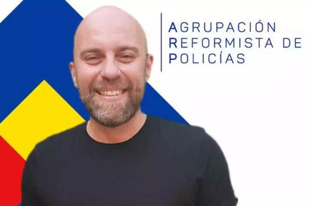 Hombre calvo con barba y camiseta negra sonriendo frente a un fondo con el logotipo de la Agrupación Reformista de Policías.