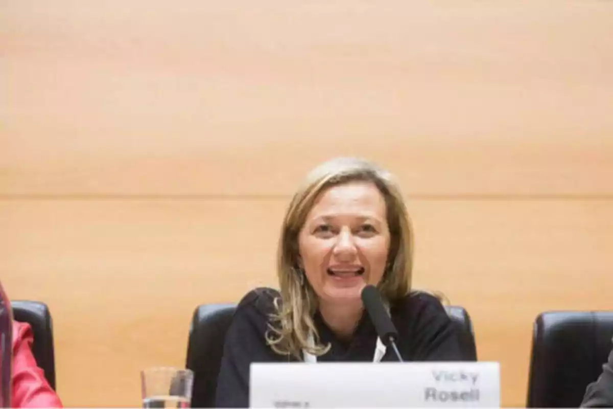 Una mujer hablando en un micrófono durante una conferencia, con un cartel que dice "Vicky Rosell" frente a ella.