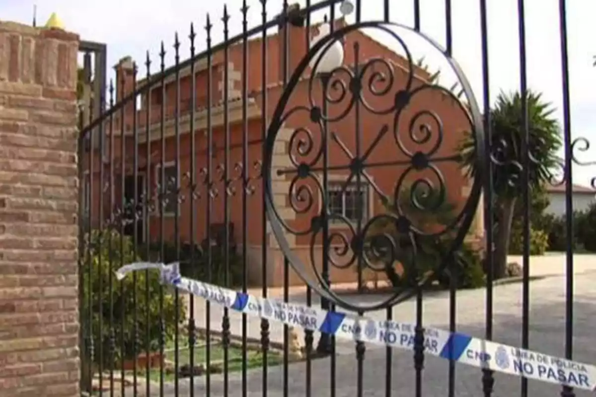 Reja de hierro con cinta de policía que dice "NO PASAR" frente a una casa.