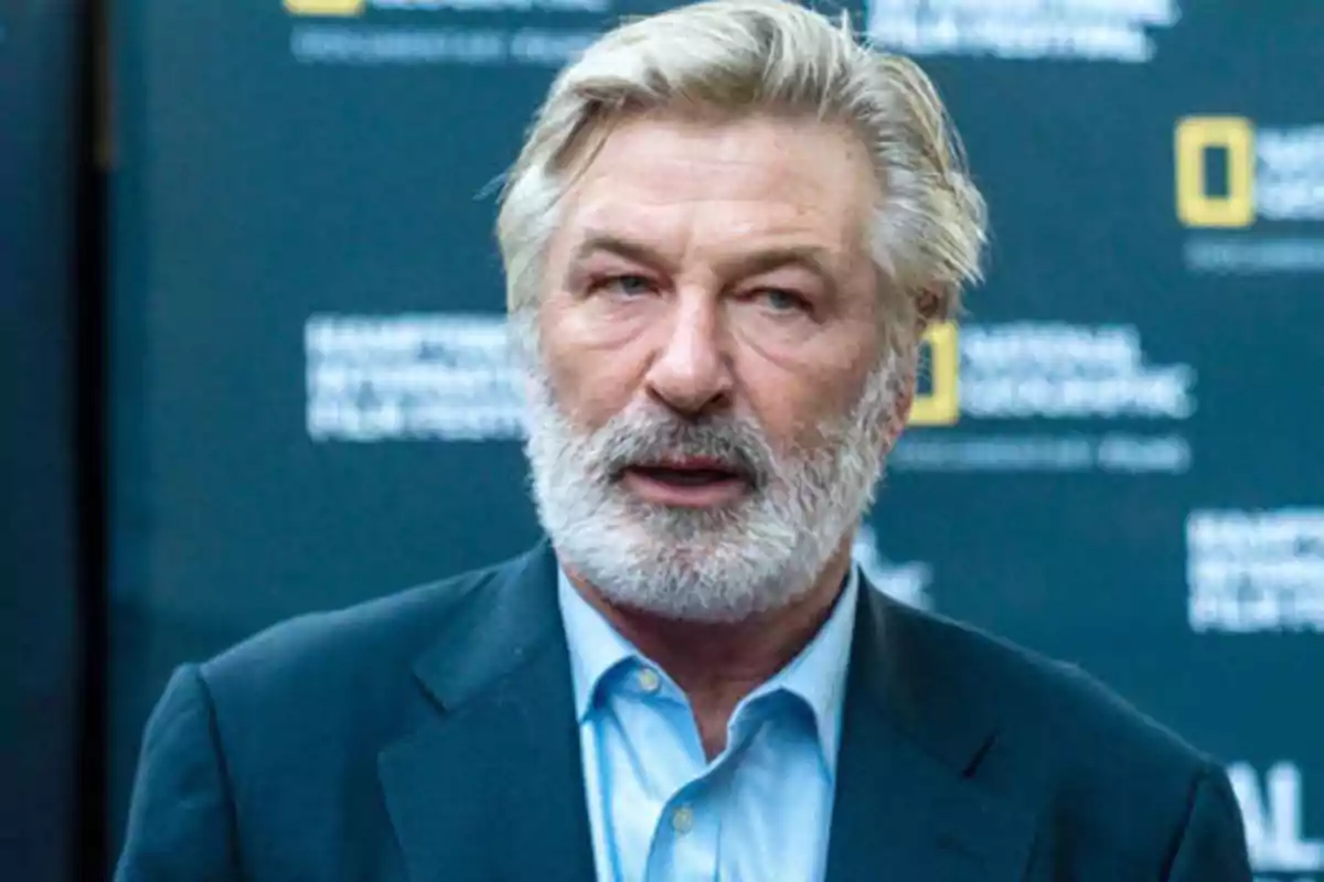 Hombre con barba y cabello canoso, vestido con traje y camisa azul, frente a un fondo con logotipos de National Geographic.