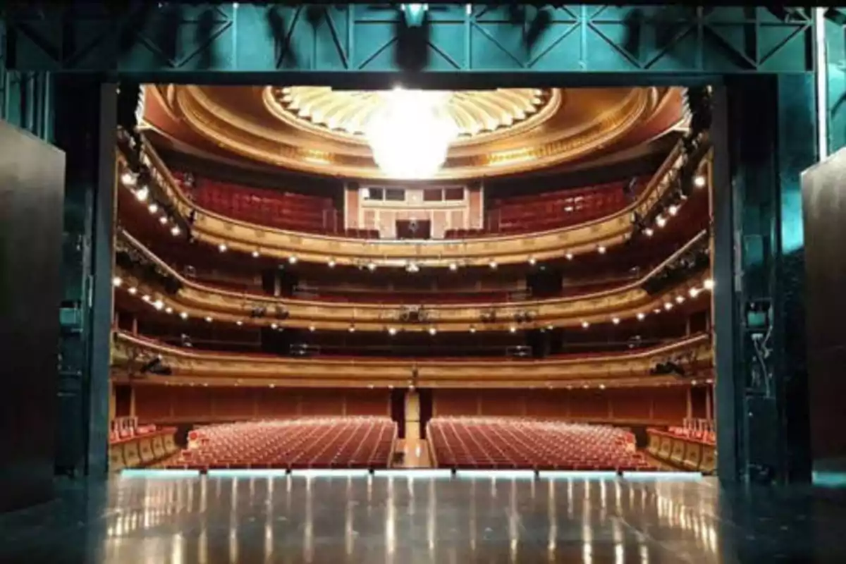 Vista desde el escenario de un teatro con varias filas de asientos y balcones iluminados.