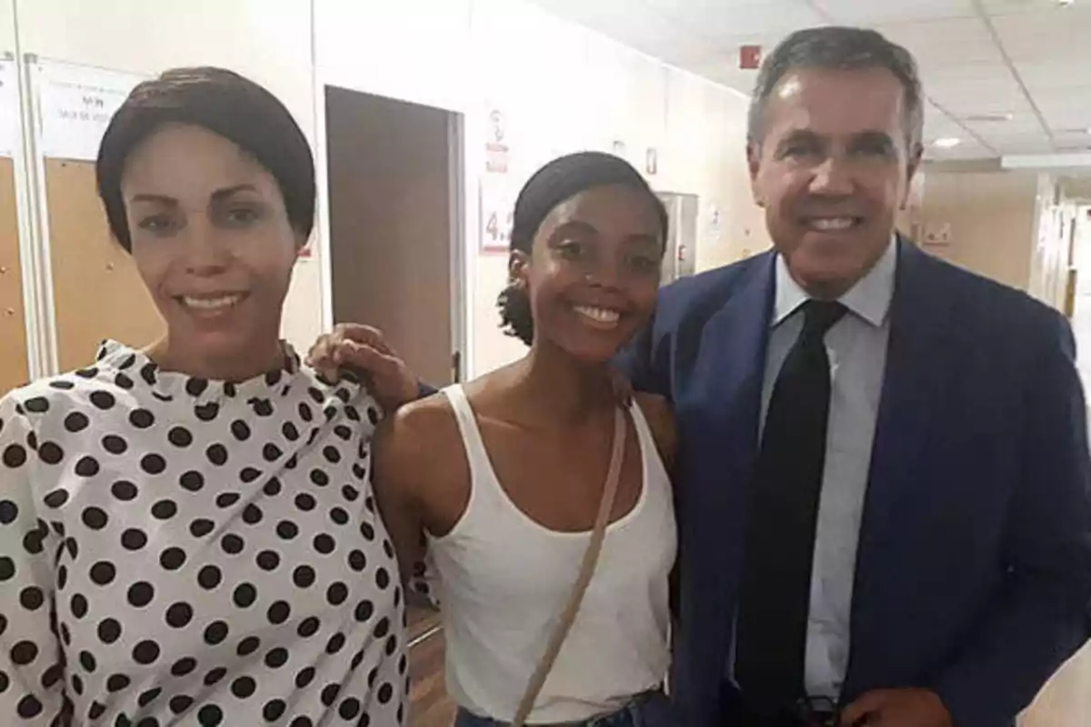 Tres personas posando juntas en un pasillo, una mujer con blusa de lunares, una mujer con camiseta blanca y un hombre con traje azul.