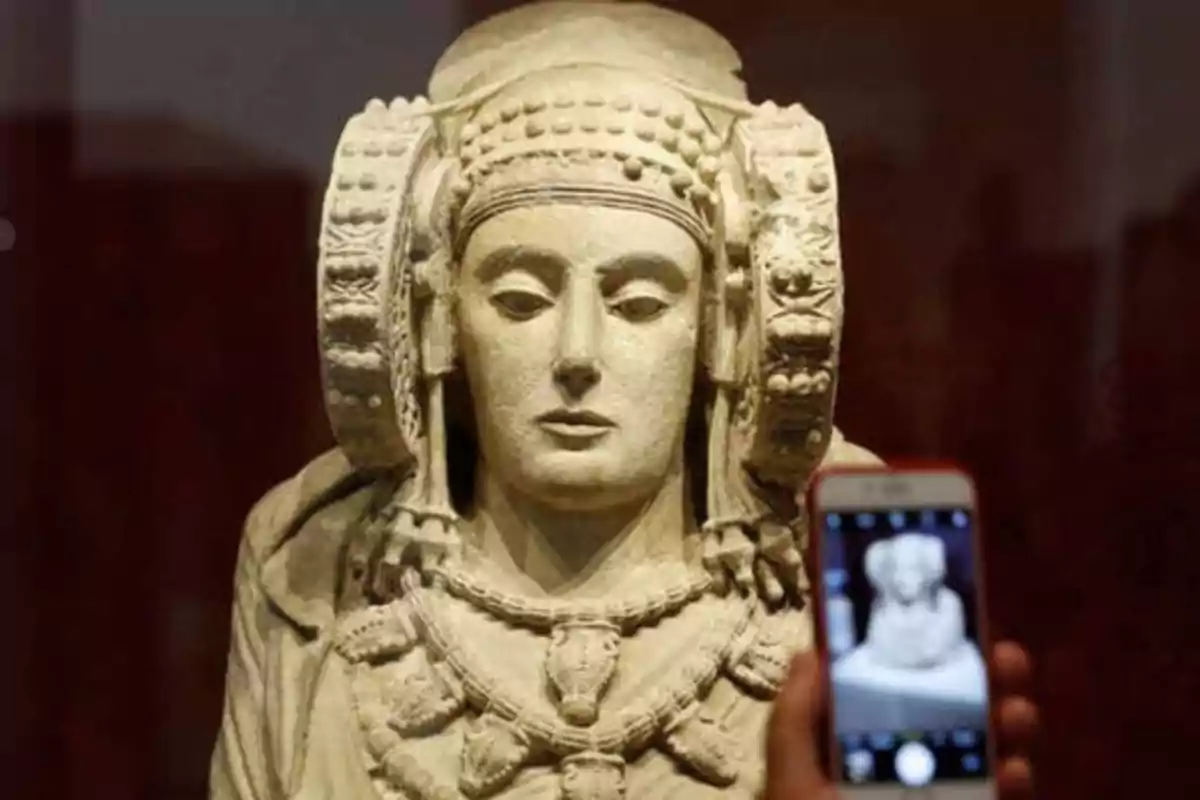 Una persona toma una foto de una escultura antigua con un teléfono móvil.